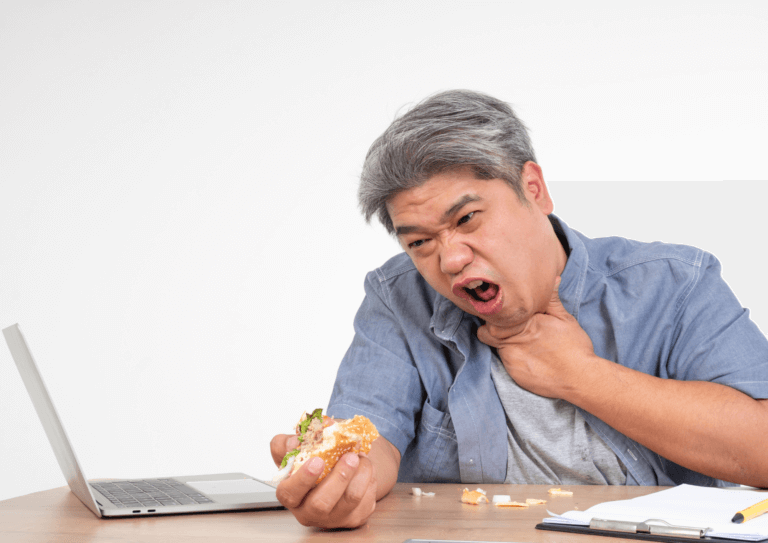 A man at his desk clutches his throat and gasps for air. His other hand still holds the food stuck in his throat: a burger.