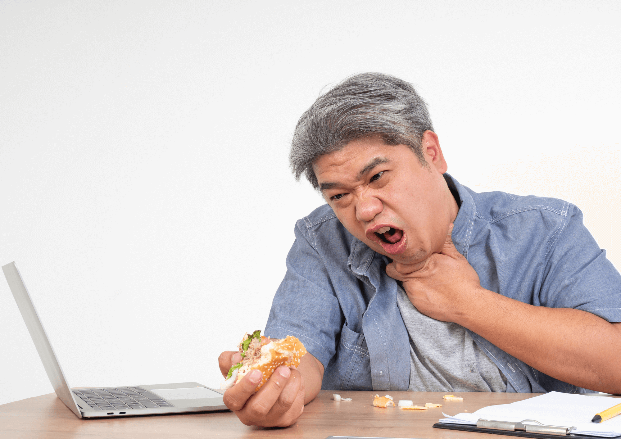 A man at his desk clutches his throat and gasps for air. His other hand still holds the food stuck in his throat: a burger.